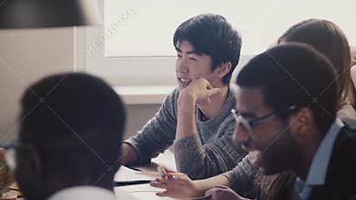 Close-up happy Japanese young employee listening and laughing together with colleagues at multiethnic office meeting.