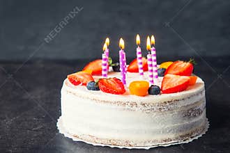 White birthday healthy yougurt cake with fresh strawberries, blueberries and candles on dark gray, black stone background. Happy h