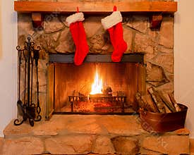 Two Christmas stockings on the mantle of a stone fireplace with a warm fire.