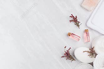 Natural spa cosmetics with pink rose oil, salt, soap and lavender flowers on white wood background, top view, border.
