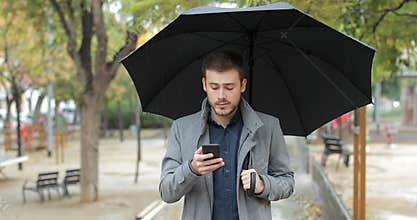 Frustrated man checking weather app on phone in a rainy day