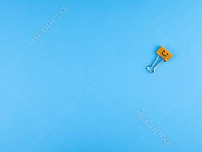Orange metal binder clip or multicolored paperclip on blue background