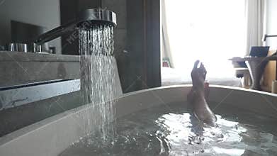 Man`s legs in a bathroom of hotel. hot water pours into the bath and from it comes steam.