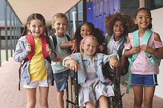 Happy school kids standing in corridor while schoolgirl sitting on wheelchair