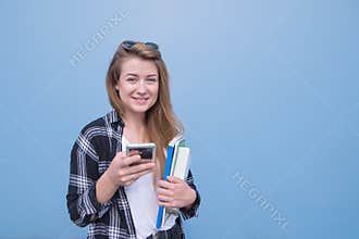 Student girl isolated on a blue background with books, notebooks and a smartphone in her hands looking at the camera