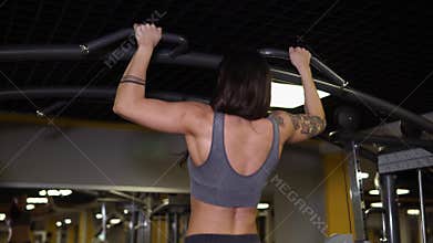 Strong woman is doing pullups in gym.