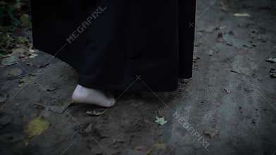 Close up shot of the feet of a woman who walks barefoot along the ground on which fall autumn leaves fallen from trees