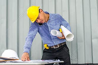 Busy construction engineer talking on phone while carrying blueprints with checking the building progress
