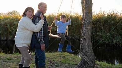 Mutual relations of child and adults, leisure of happy people near river among reeds in bright sunlight