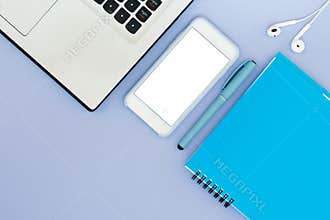 Layout with a laptop, phone, notepad and headphones on a blue background. Place for text. Flat Lay Desktop Tools Layout.