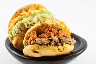 Arepas filled with shredded beef and pork rind served in a black ceramic dish