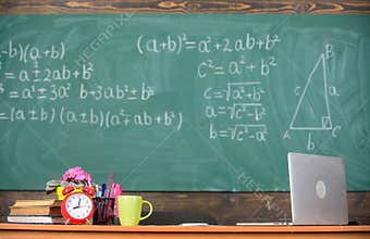 Teachers attributes. Table with school supplies alarm clock books and mug classroom chalkboard background. Working