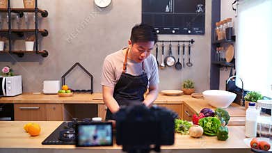 Young asian man in kitchen recording video on camera. Smiling asian man working on food blogger concept with fruits and vegetables