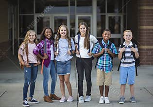 Group portrait of pre-adolescent school kids smiling in front of the school building