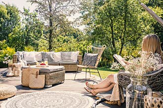 Woman reading book while relaxing at terrace with rattan furniture in the garden. Real photo