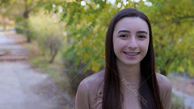 Smiling teenager girl with braces looking around and at the camera outside