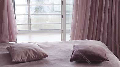 Four decorative pillows falling on bed. Someone throws cushions on sofa. Cozy interior with large window and curtains in