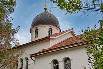 White-stone orthodox church with golden domes and crosses through the branches of trees around in summer. Religion and faith