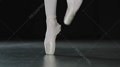 Ballerina female legs close-up dancing jumping standing on tip-toes ballet position practicing rehearsing on parquet