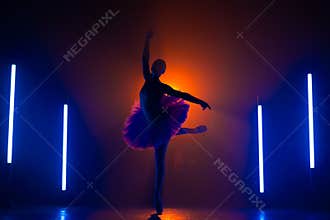 Silhouette of ballerina is practicing elements in studio with neon colorful light. Young woman dancing in classic tutu