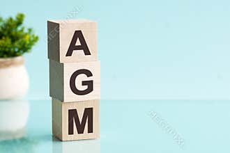 AGM - Annual general meeting - acronym on wooden cubes on blue backround. Business concept