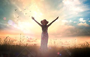 Woman in Floral Dress Raising Arms toward Flying Birds and Golden Sunset in Meadow