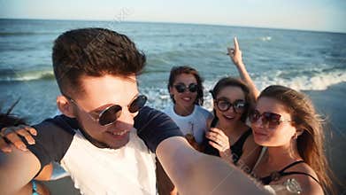 Pov view of young friends taking selfie having fun with drinks on sea beach on sunset. Online video call: man looking at