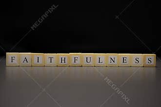 The word FAITHFULNESS written on wooden cubes isolated on a black background