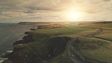 Sun green fields, meadows aerial. Cars drive at road. Ireland hills, farmlands at cloudy day