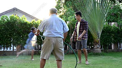 Grandfather water the plants in garden and playing with family. Retirement age lifestyle with family on backyard