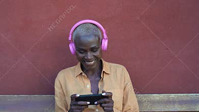 Happy African woman using mobile smartphone while listening music with headphones