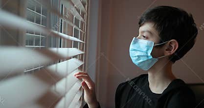 A boy with a protection mask looks out the window. Coronavirus, Covid-19.