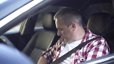 Close-up of confident middle aged Caucasian man fastening seat belt sitting on driver's seat and turning on engine