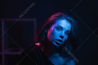 Night neon portrait of a stylish beautiful woman with makeup with glitter in blue and purple light on the party, looking at the