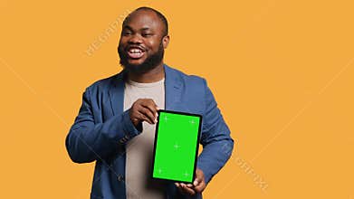 Amused man laughing while presenting tablet with green screen display