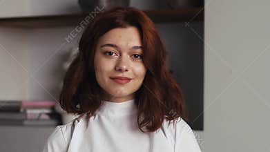 Portrait of Beautiful Young Woman with Red Hair Wearing white Sweater Looking Up to the Camera and Smiling Charmingly