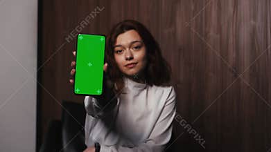Woman Holding Mobile Phone Green Screen. female shows smartphone chroma key. Smiling lady looking at camera at home or