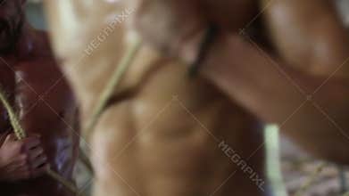 Breasts of five sweaty men pull ropes in abandoned