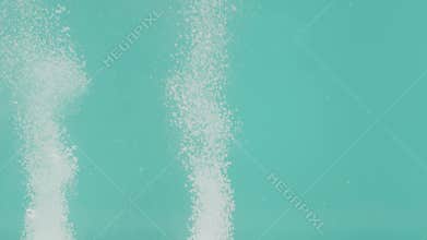 The pair of white effervescent pills on a turquoise background lie at the bottom of the container and dissolve in water
