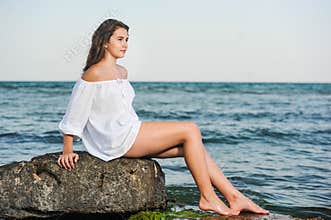 Caucasian teen girl in bikini and white shirt lounging on lava rocks by the ocean