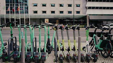 Green Electric Scooters And Bikes Parked On Sidewalk In Urban Area