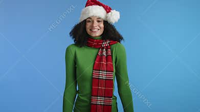 Amused young cute woman in xmas hat dancing, shaking head on blue background