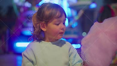 Beautiful and happy little girl eating pink cotton candy in the park