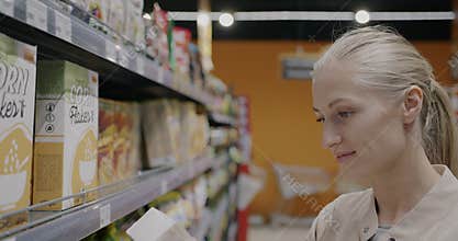 Cheerful young woman buying muesli in grocery store choosing organic food taking carton from shelf in supermarket