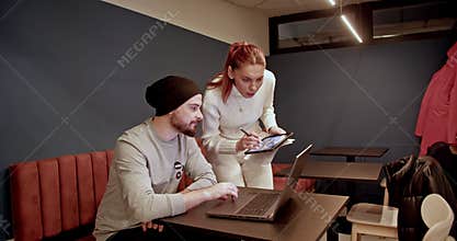 Two young adults collaborate on a project using technology in a modern workspace.