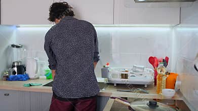 Caucasian Man Carrying Plate Toward Sink In Tidy Kitchen, Rinsing Pans And Placing Dishes By Faucet, Casual Shirt, Focused