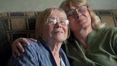 Elderly mother and adult daughter embracing together at sofa