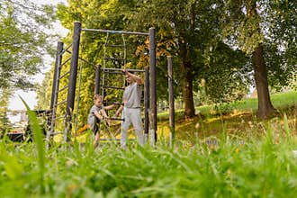 A father and his child share joyful time at a playground, engaging in fun activities together. The vibrant green trees and sunny