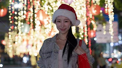Young Asian Woman In Santa Hat At Christmas Market Looking at Camera