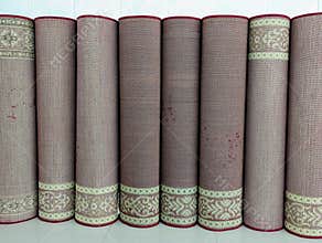 Rolled rugs with decorative borders stand vertically in a row indoors